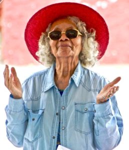 Elderly woman in hat and sunglasses with outstretched hands